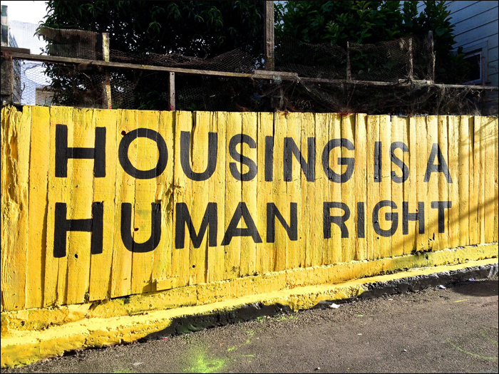 Housing is a human right painted on yellow wall in community street