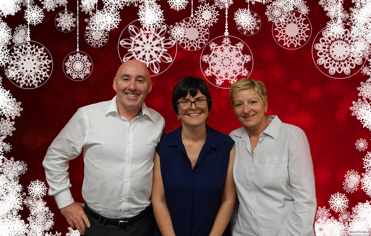 Paul, Jemima and Julie, standing in front of red background with snowflake design