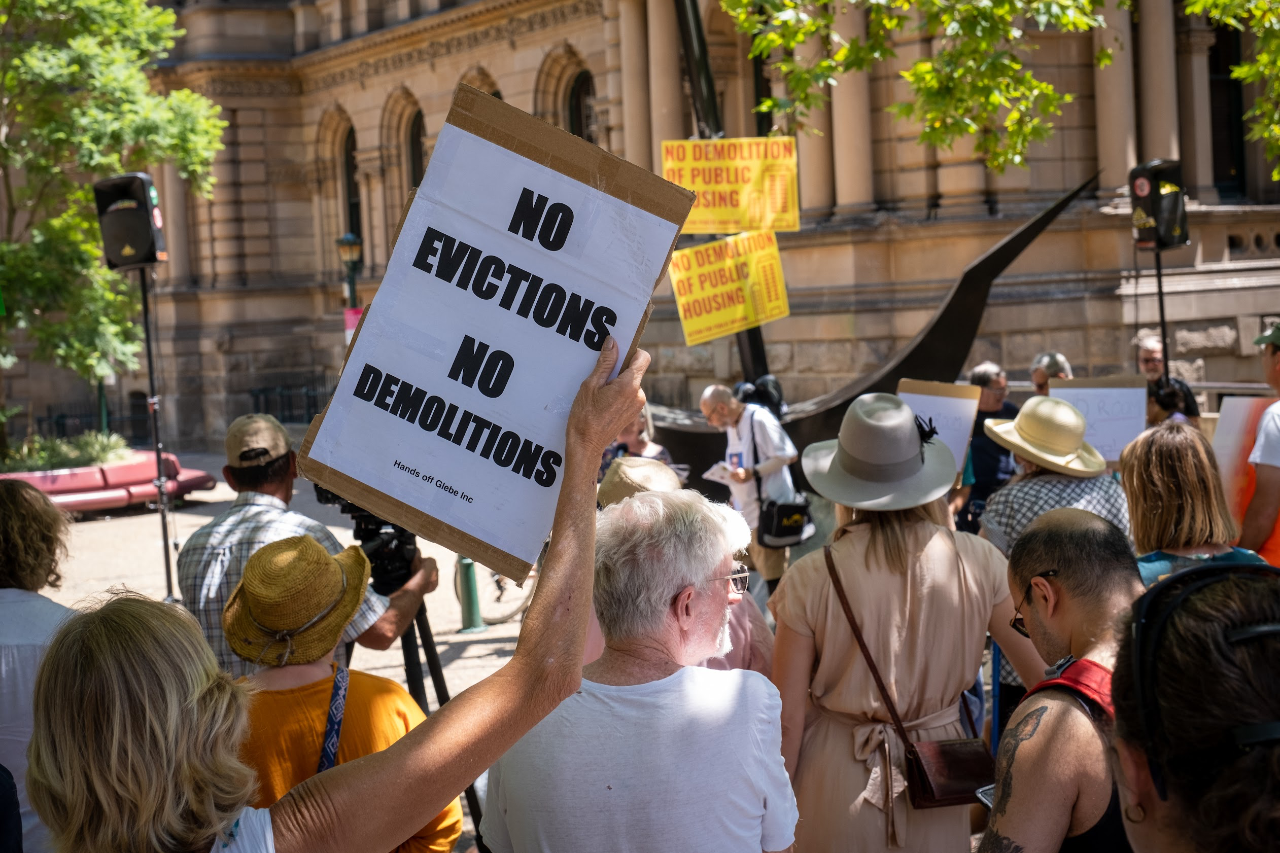 A woman holds a sign saying no evictions no demolitions with other protestors outside Sydney Town Hall