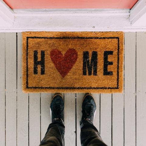 Home, two feet at a door mat that reads 'home' leading in to a house