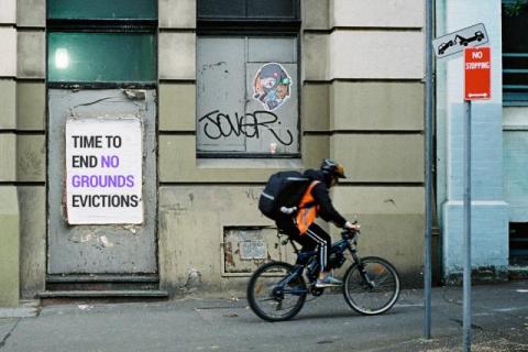 Person riding a bike past a poster with the words 'time to end no grounds evictions'
