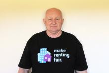 A man wearing a Make Renting Fair t-shirt smiles at the camera