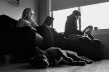 A black and white photo of two people and a dog in a lounge room